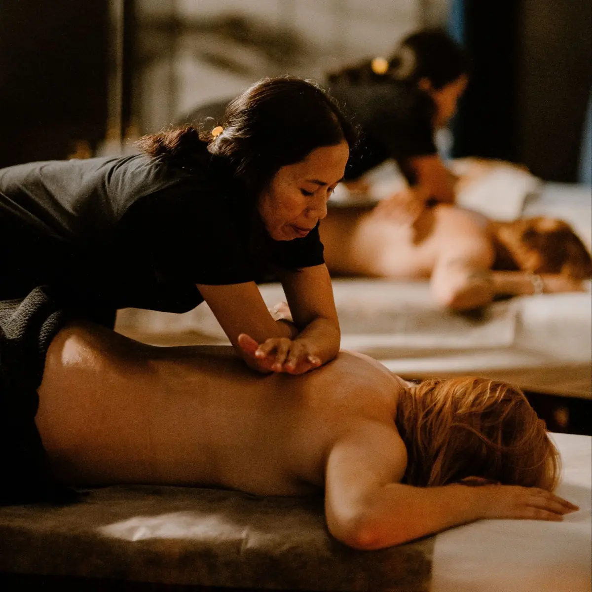 Couples massage at Tera Thai: a therapist massages a guest's back, with a second therapist at the next table behind her